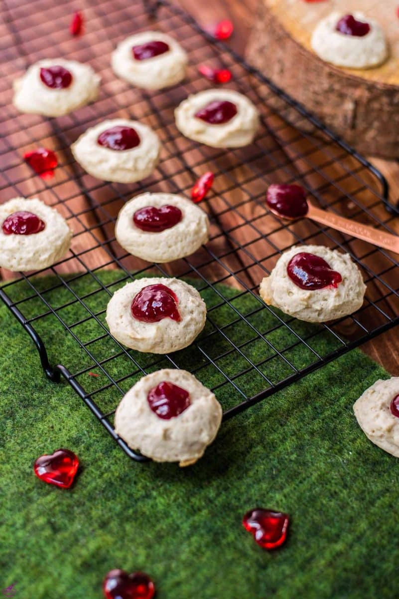 Gorgeous raspberry cream cheese thumbprint cookies on black cooling rack.