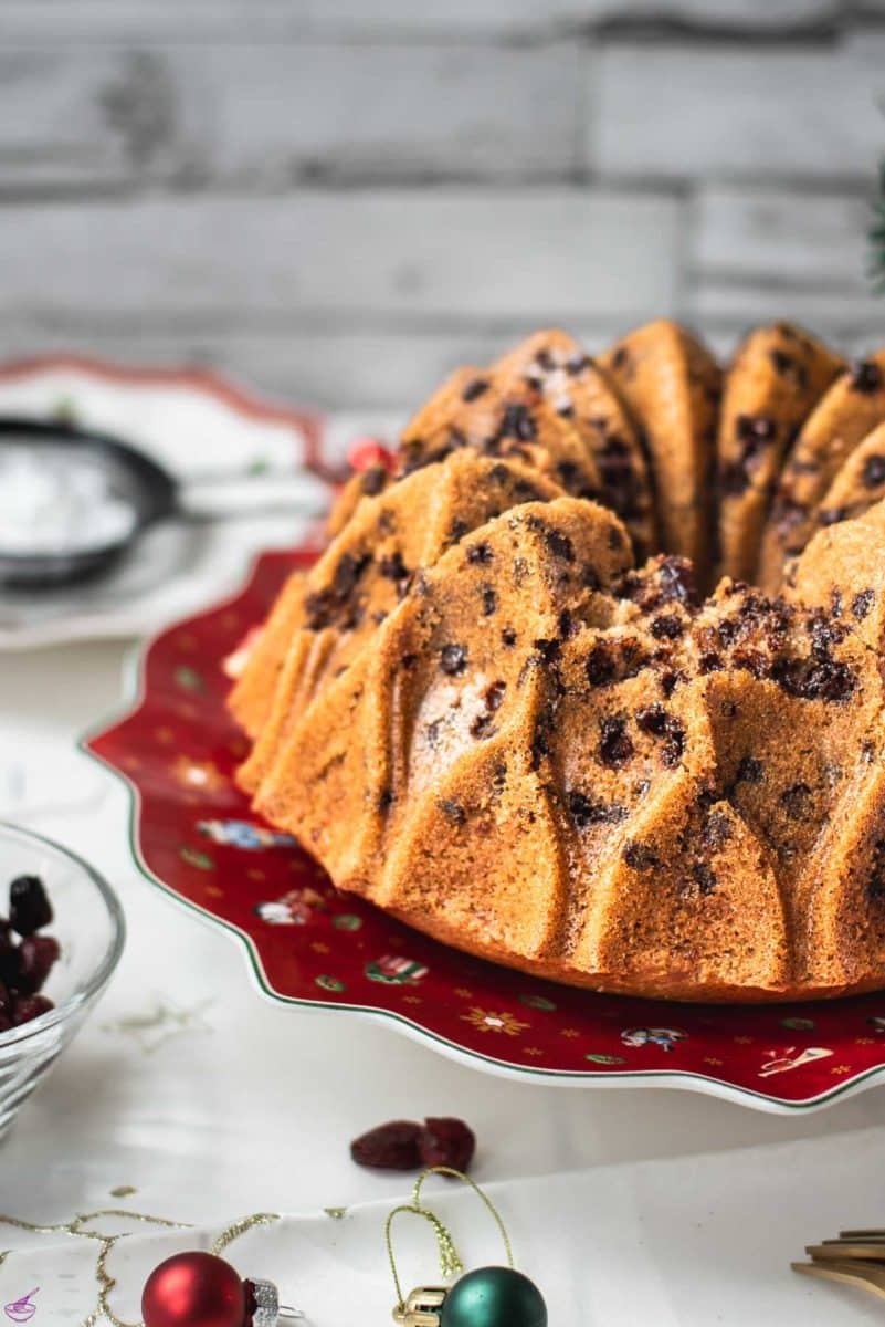 Gorgeous cranberry bundt cake with chocolate chips, cinnamon, and of course dried cranberries. Placed on a red plate.