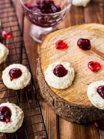 Gorgeous raspberry cream cheese thumbprint cookies on black cooling rack and wooden board.