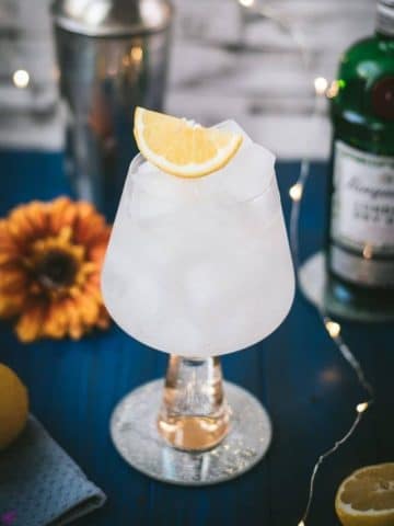 Gorgeous glass filled with a refreshing lemon gin and tonic. Placed on blue wooden ground.