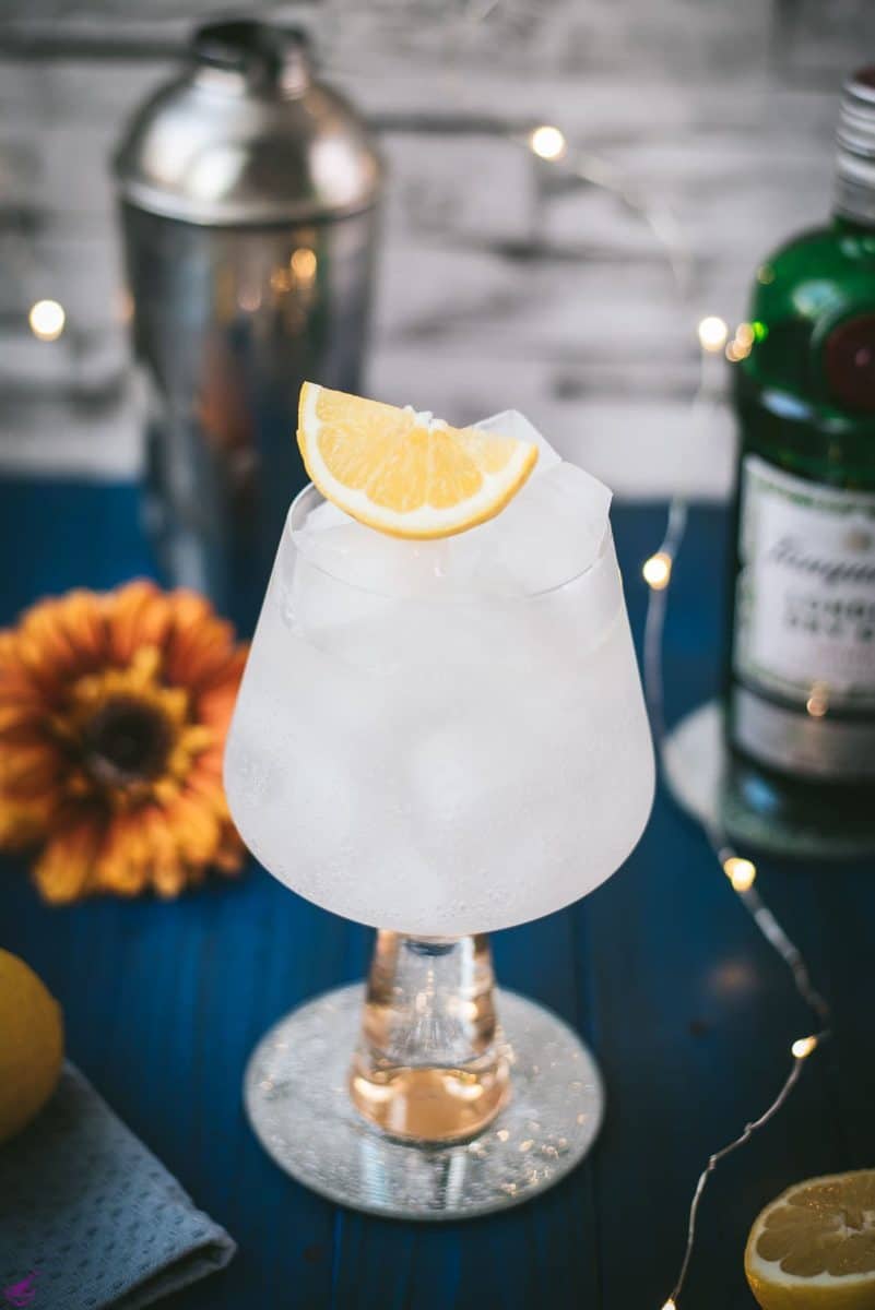 Gorgeous glass filled with a refreshing lemon gin and tonic. Placed on blue wooden ground.