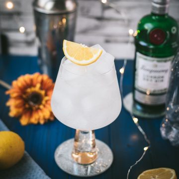 Gorgeous glass filled with a refreshing lemon gin and tonic. Placed on blue wooden ground.