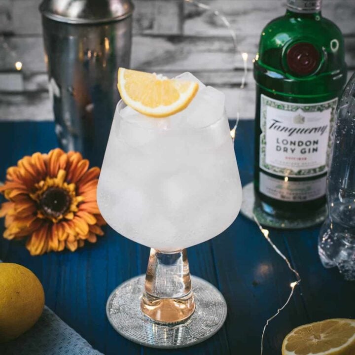 Gorgeous glass filled with a refreshing lemon gin and tonic. Placed on blue wooden ground.