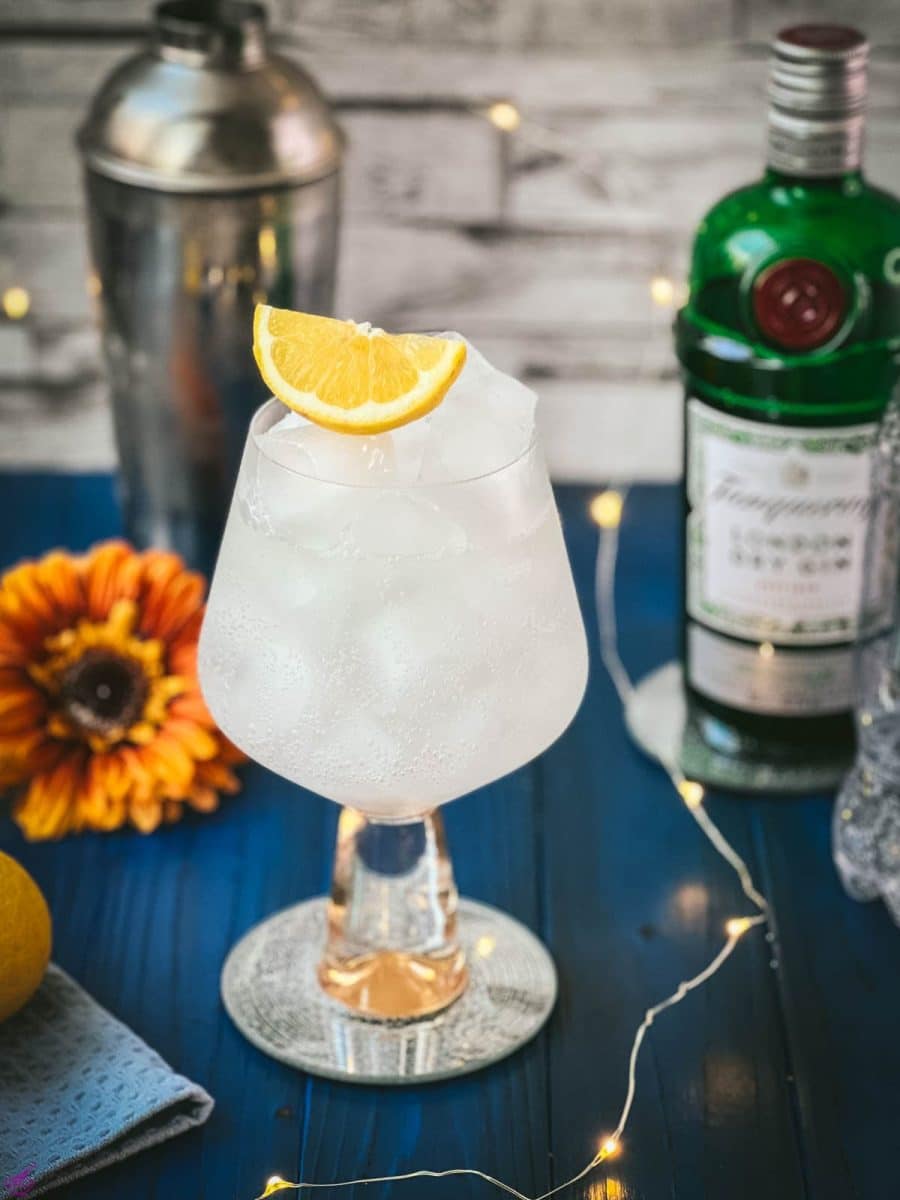 Gorgeous glass filled with a refreshing lemon gin and tonic. Placed on blue wooden ground.