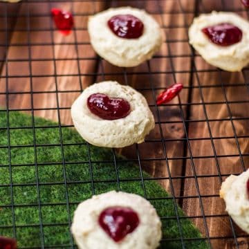 Gorgeous raspberry cream cheese thumbprint cookies on black cooling rack.