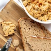 white bowl with liptauer on white ground next to cuttingboard with bread slices