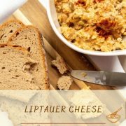 white bowl with liptauer on white ground next to cuttingboard with bread slices