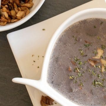 white soup bowl with chestnut porcini mushroom soup on dark ground with roasted porcini mushrooms in a second bowl and on a plate