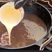 dutch oven on the grill with chestnut soup inside - gloved hand is pouring whipped cream into the dutch oven