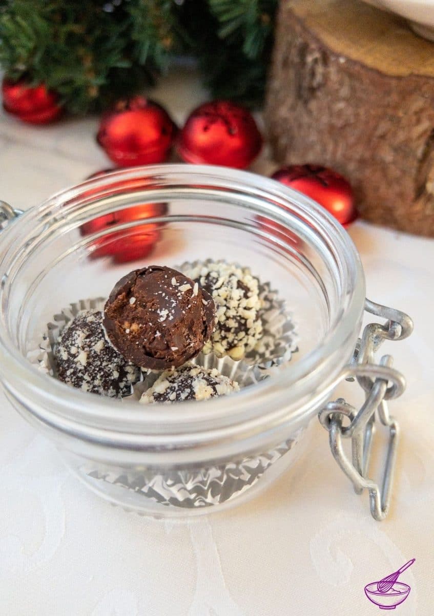 Orange Marmalade Truffles with Dark Chocolate rolled in minced almonds on white tablecloth. Christmas decoration in the back.