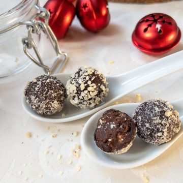 Orange Marmalade Truffles with Dark Chocolate rolled in minced almonds on white tablecloth. Christmas decoration in the back.