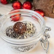 Orange Marmalade Truffles with Dark Chocolate rolled in minced almonds on white tablecloth. Christmas decoration in the back.