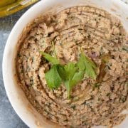 homemade hummus in a bowl next to olive oil and tableware