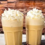 two glasses filled with creamy iced coffee, garnished with whipped cream.