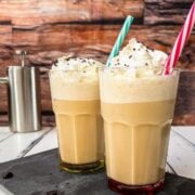 two glasses filled with creamy iced coffee, garnished with whipped cream and chocolate sprinkles. Colorful straws to drink from.