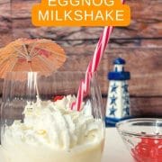 Glass with homemade eggnog milkshake, topped with whipped cream and a yummy cocktail cherry on top.