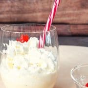 Glass with homemade eggnog milkshake, topped with whipped cream and a yummy cocktail cherry on top.