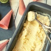 Loaf pan filled with homemade vanilla ice cream and scooped out vanilla icecream. With pink ice cream cones alongside.