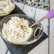 Glass serving bowl with pineapple, whipped cream, and chocolate sprinkles on black stone plate.