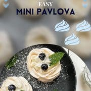 Meringue nests filled with whipped cream, decorated with blueberries and mint leaves, and dusted with powdered sugar. Placed on black serving plate.