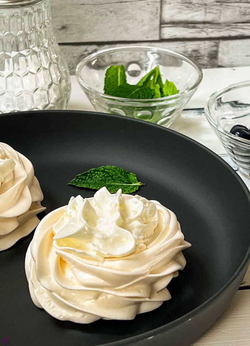 Meringue nests filled with whipped cream. Placed on black serving plate. 