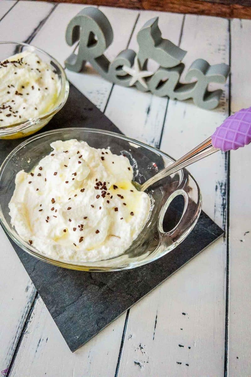 Glass serving bowl with pineapple, whipped cream, and chocolate sprinkles on black stone plate.