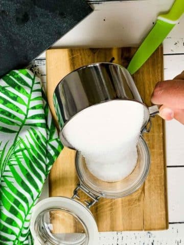 Pouring in a cup of granulated sugar into a preserving jar.