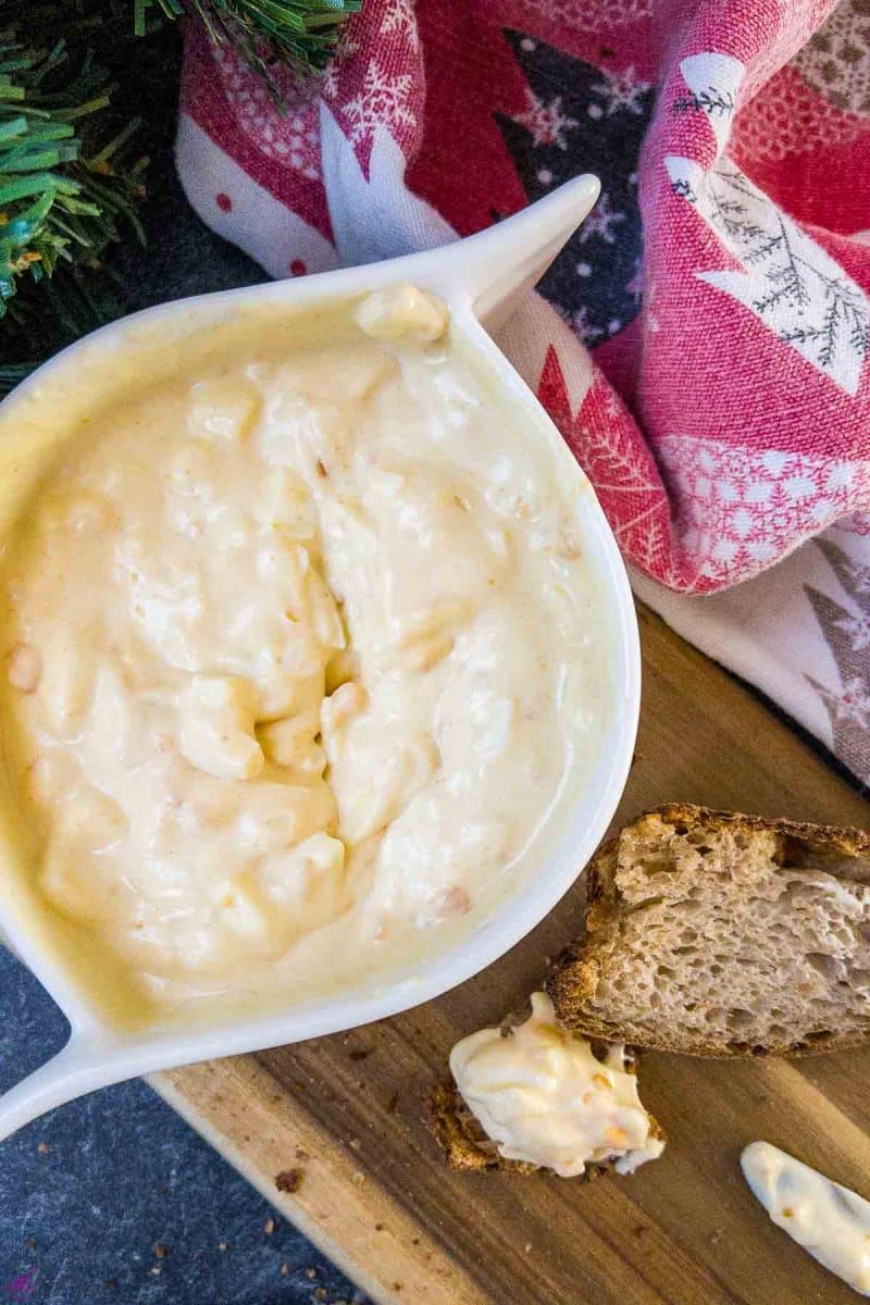 White bowl with egg salad spread and coated bread on brown board.