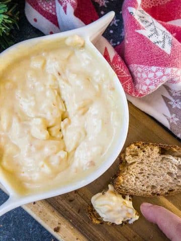 White bowl with egg salad spread and coated bread on brown board.