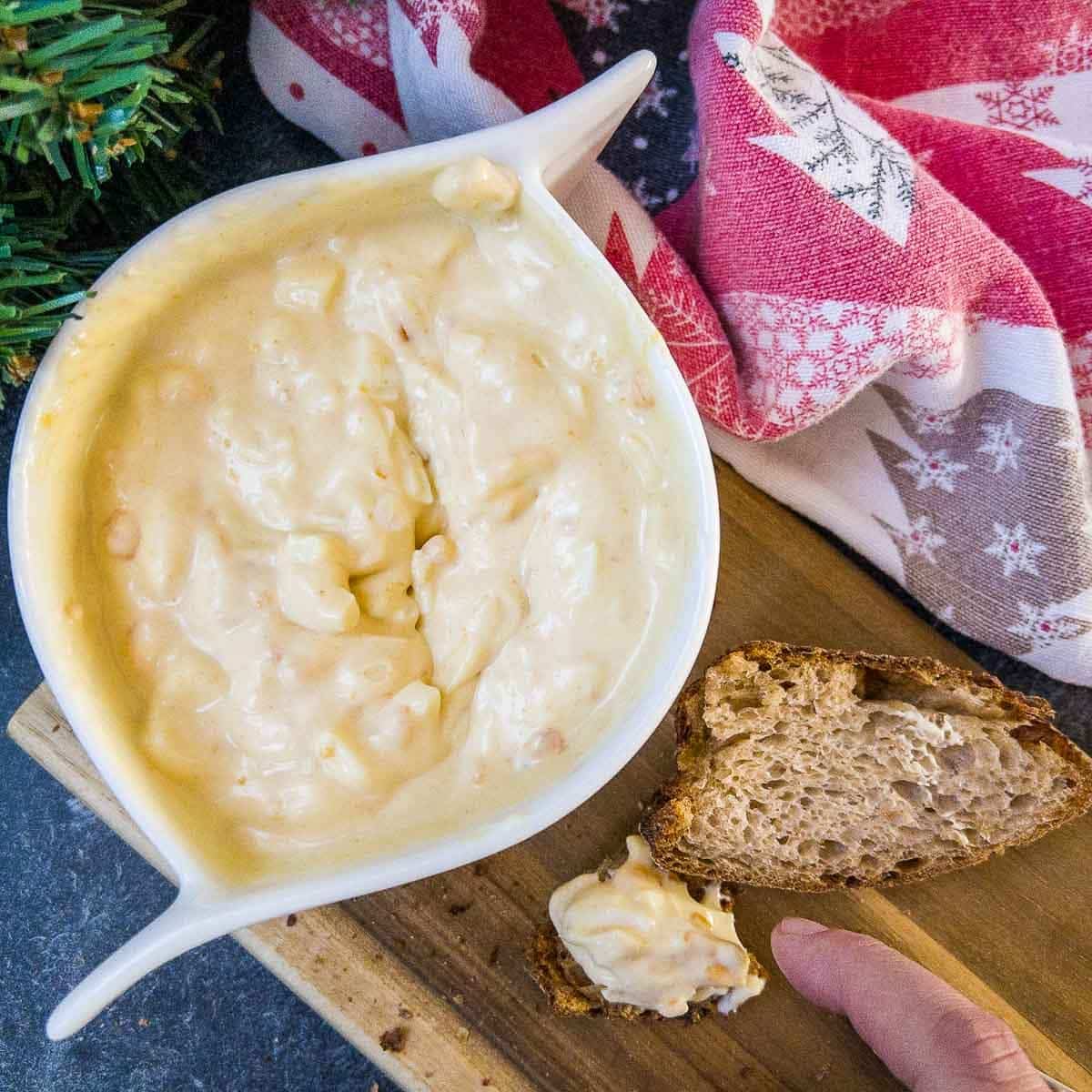 White bowl with egg salad spread and coated bread on brown board.