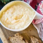 White bowl with egg salad spread and coated bread on brown board.