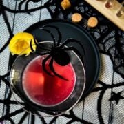 Blood red Halloween cocktail in glass decorated with spider. Black serving plate and spider web decoration.
