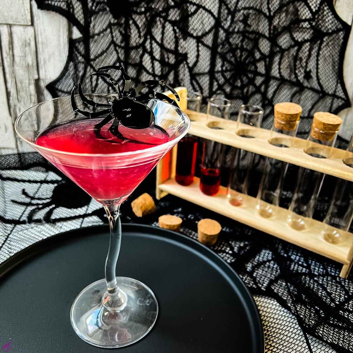 Blood red Halloween cocktail in glass decorated with spider. Black serving plate and spider web decoration.