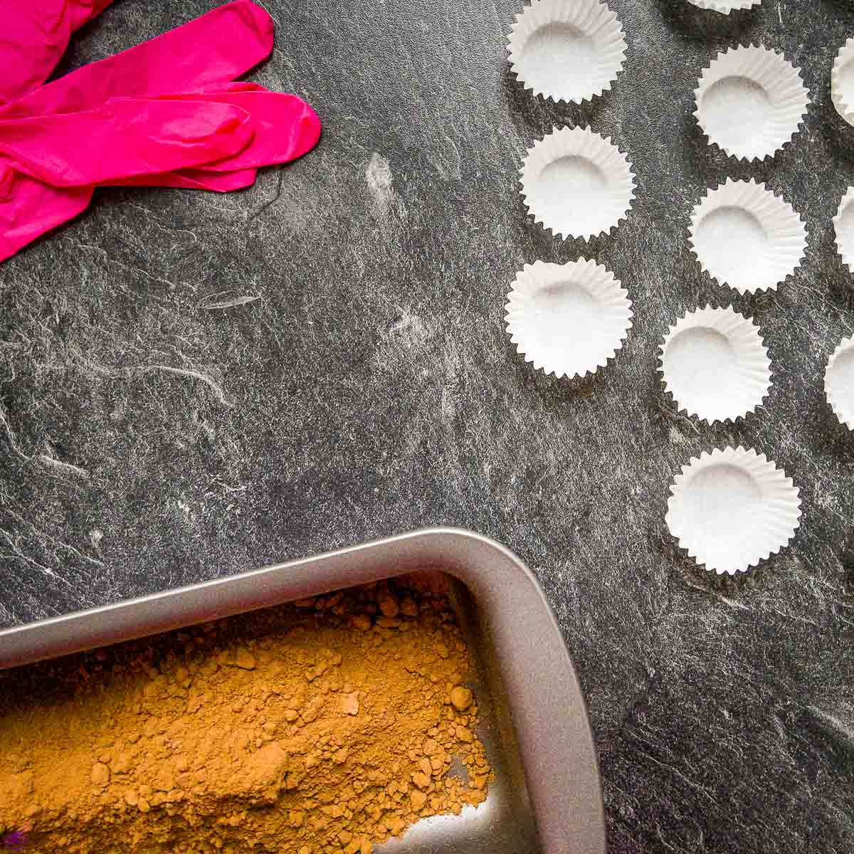 Chocolate paper cups, disposable gloves, and pan with raw Criollo cacao powder.