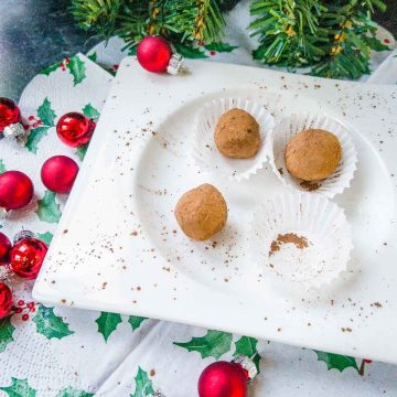 Scrumptious Biscoff truffles on white plate. Decorated with red Christmas baubles on the side.