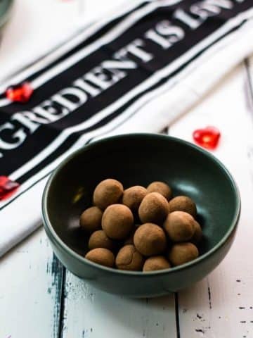 Delicious marzipan potatoes in a dark green bowl on white wooden ground.