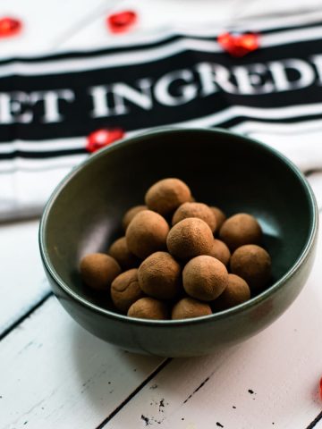 Delicious marzipan potatoes in a dark green bowl on white wooden ground.