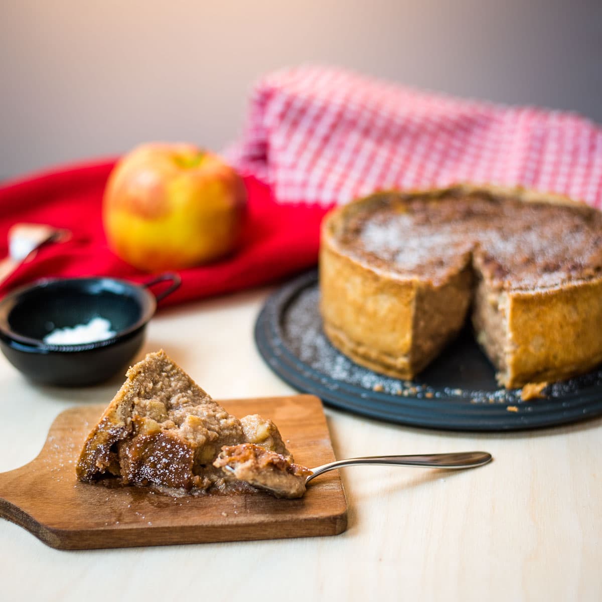 Delicious slice of a luscious apple tart, placed on a wooden cutting board, with a spoon beside.