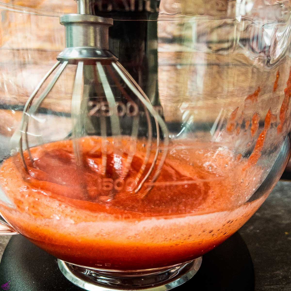 Glass bowl with whisk mixing puréed strawberries.