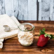A Weck glass filled with strawberry flavored whipped cream, next to a gorgeous red strawberry.