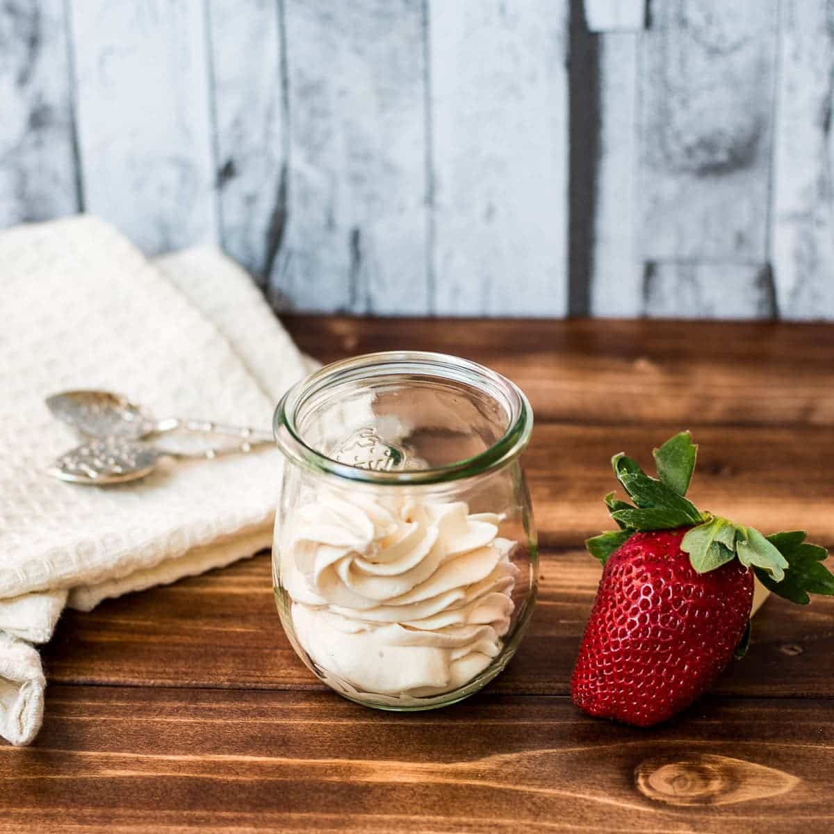 A Weck glass filled with strawberry flavored whipped cream, next to a gorgeous red strawberry.