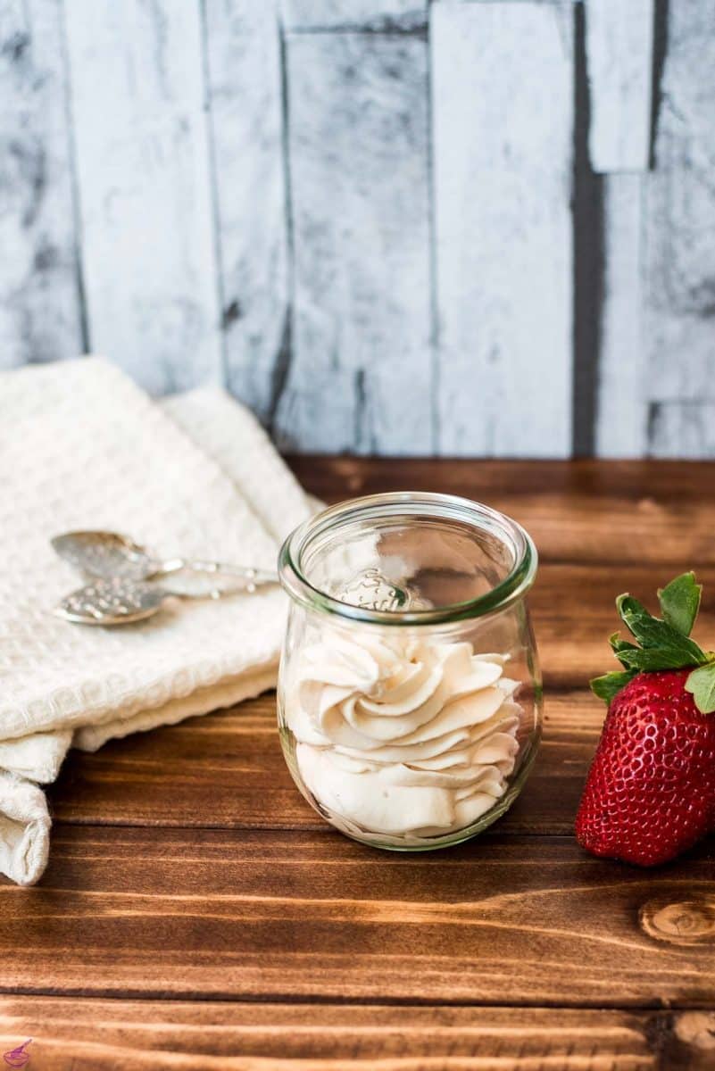 A Weck glass filled with strawberry flavored whipped cream, next to a gorgeous red strawberry.