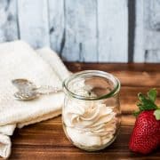 A Weck glass filled with strawberry flavored whipped cream, next to a gorgeous red strawberry.