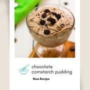 Beautifully textured chocolate cornstarch pudding in a dessert glass. Placed on a wooden coaster on a white wooden floor. Decorated with small pieces of cookies.