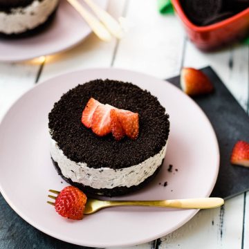 Mini no-bake Oreo cheesecake on a pink plate decorated with sliced strawberries.