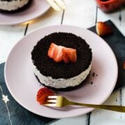 Mini no-bake Oreo cheesecake on pink plate, decorated with sliced strawberries.