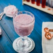 Cute and delicious pink strawberry milk in a gorgeous serving glass. Placed on a glass coaster on blue wooden ground.