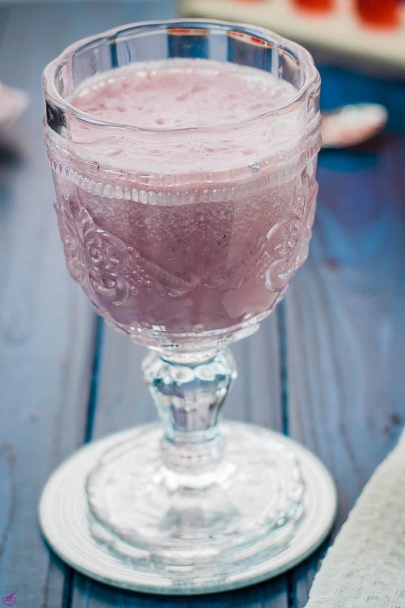 Cute and delicious pink strawberry milk in a gorgeous serving glass. Placed on a glass coaster on blue wooden ground.