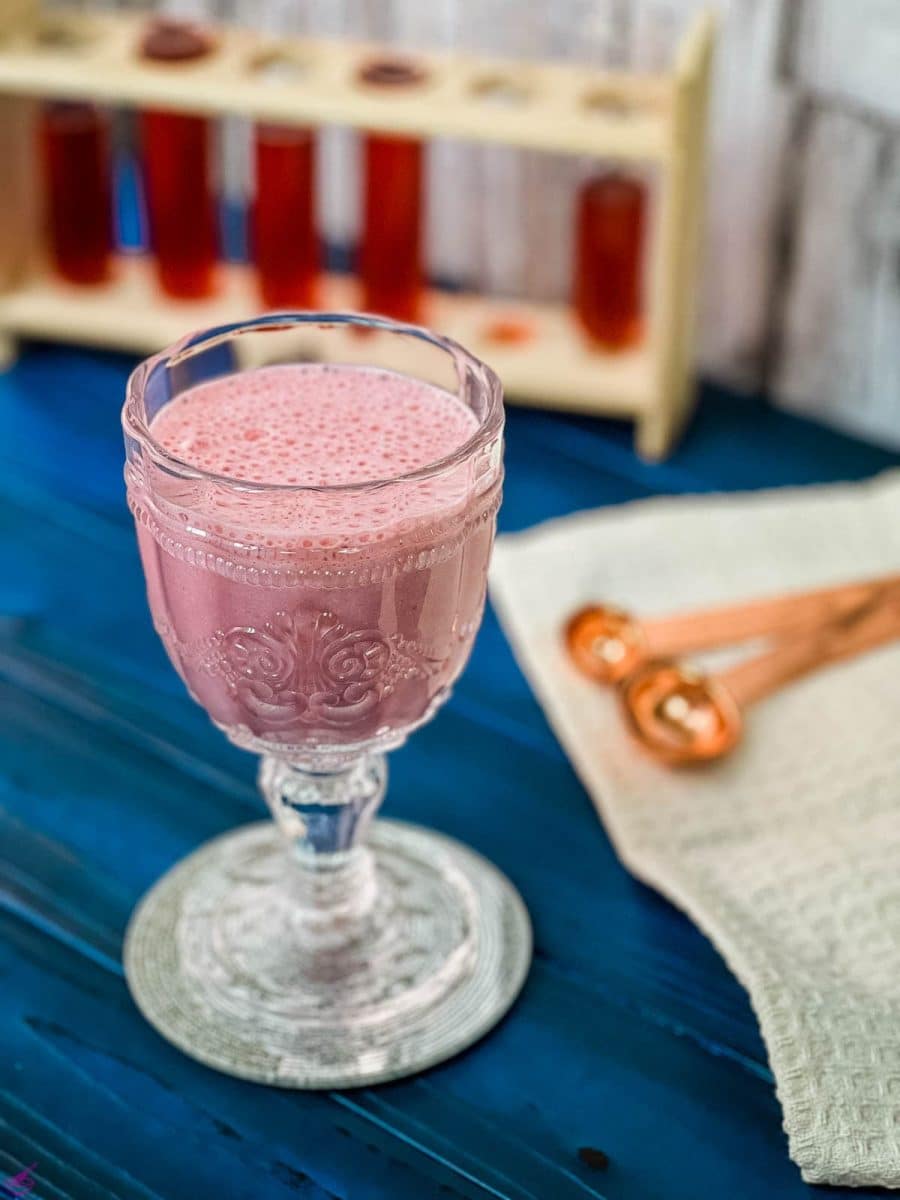 Cute and delicious pink strawberry milk in a gorgeous serving glass. Placed on a glass coaster on blue wooden ground.