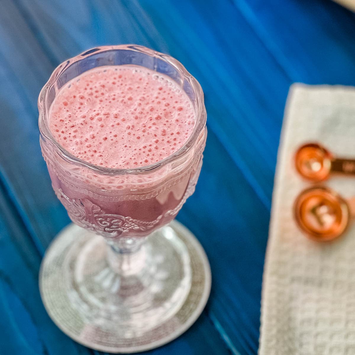 Cute and delicious pink strawberry milk in a gorgeous serving glass. Placed on a glass coaster on blue wooden ground.